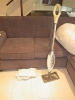 Full view of the Shark Professional steam mop standing upright next to a sofa with four washable mop pads placed on the floor beside it.
