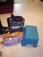 View of lot showing black Bell and Carrera helmets inside a reusable bag, purple and orange children's folding chairs rolled up, blue plastic step stool