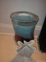 Tall ceramic vase with blue and brown glaze, smooth curved sides, signed Svaja, photographed on floor near wall