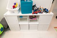 Front view showing full shelving unit with drawers, cupboards, and bins, topped with toys and containers.