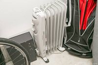 Angle view of Garrison white oil-filled radiator heater along with other miscellaneous items (black box, golf bag, bike wheel) showing heater size and design.