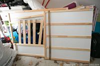 Disassembled bed frame parts including a slatted side panel and white melamine panel framed in pine wood.