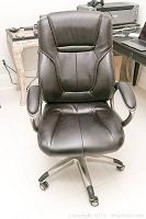Front view of the black vinyl office chair showing padded backrest and seat with metal frame base and casters.