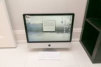 Front view of Apple iMac powered on, showing 24-inch display, aluminum chassis, white Magic Keyboard positioned in front, lot sticker #621 on bezel.