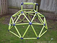 Photo of lime green jungle gym dome with blue joints standing on grass near wooden fence.