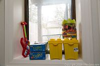 Full lot arranged on a window ledge showing toy guitar, two Zingo game boxes, three yellow bins, and clear jar of LEGO Bristle Blocks.