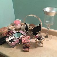 Photo showing various decorative boxes, small containers, wicker basket with handle, manicure scissors, pink and patterned trinkets, and the glass vase with silver rim on tabletop.