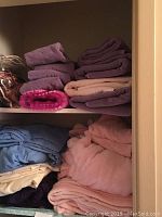 Folded towels and queen bedding on shelves in various pastel and dark colors