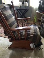 Side view of wooden rocking chair with padded striped seat cushion showing armrests and rocking base.