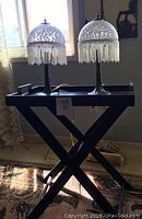 Photo showing wood serving table and two vintage style lamps with white mottled glass shades and beaded fringes, with the Eiffel Tower canvas visible in the background.