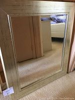 Wall mirror standing upright against a door reflecting part of a room with carpet and furniture