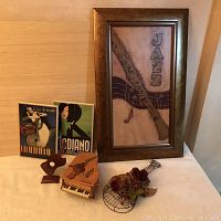 Photo of framed jazz art piece with wooden carved clarinet and music notes along with two vintage-style posters and small wooden musical sculptures on white surface.