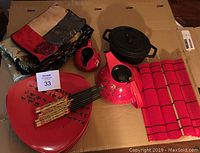 Lot with folded placemats, teapot, creamer, chopsticks, plates, cast iron pot on cardboard