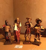 Four paper mache figurines, each approximately 10-12 inches tall, arranged side by side, showing detailed painted features and clothing.