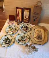 Full lot overview showing 4 decorative wine-themed cheese plates, an octagonal platter, two rectangular plaques, fabric wine bottle tote, silver cherub figure, and wine cork holder arranged on floor.