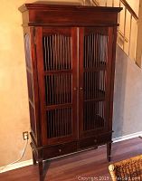 Front view of the wooden cabinet showing slatted panel doors, two drawers, and tapered legs