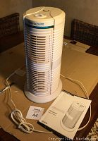 White Therapure tower air purifier with control dial on top, power cord laid out, and user manual beside it, all placed on cardboard surface.