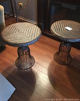 Photo showing two round rattan topped end tables with black metal bases on hardwood floor.