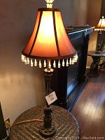 Full view of one illuminated lamp with brown fabric shade and hanging beads, showing height and style.