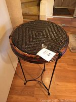 Photo showing the round woven rattan tabletop and metal base of the table from a top-down angle.