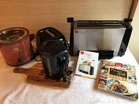 Photo showing Ronco Ready Grill with manual and cookbook, black two-slot toaster, black electric kettle, and brown crock pot placed on a wooden board on white surface.