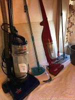 Photo showing Bissell Easy Vac, red Dirt Devil vacuum, Spin Broom, and mops standing in row.
