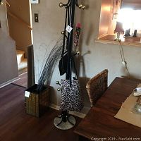 Wide view of coat rack standing next to wall and dining table, displaying leopard print bag and floral umbrella cover on hooks, also showing marble-style base.
