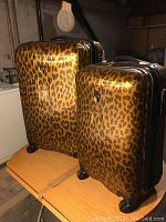 Two leopard print hard sided luggage pieces placed side by side on a table, showing the exterior in good condition with some scuff marks.