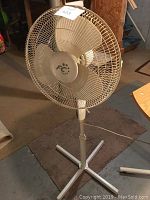 Front view of FC floor fan showing brand logo, metal grill, three blades, and adjustable stand.