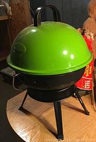 Green dome barbecue grill closed with handle on top and tripod legs