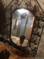 Full front view of oval mirror showing metal frame with decorative leaves and butterfly shapes.