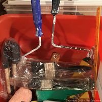 Two blue-handled paint rollers and several paint brushes sealed in plastic, plus two sponge applicators inside an orange tub.
