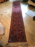 Full view of the long narrow red runner rug on a hardwood floor showing its full length and pattern.