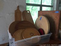 Photo showing a plastic bin filled with various wooden cutting boards of different sizes and shapes including round, rectangular and paddle-shaped boards.