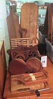 Various wooden cheese boards and decorative wooden trivets arranged together, showcasing size and style variations.