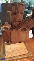 Full view of seven teak wooden trays and cutting boards, including segmented and smooth pieces, plus wooden board with slicing wire attached.