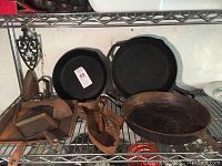 Cast iron skillets including round skillets, fish mold, square griddle, trivet, small square pan, and button hook on a metal rack.