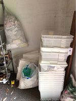 Stack of approximately 20 clear plastic storage bins with lids, some lids partially fitted, with packing materials in bags beside them.