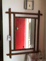 Full view of rectangular wall mirror with bamboo-style frame hung on light wall showing reflective glass and wood-textured frame.