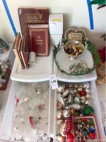 Photo showing vintage Christmas books displayed alongside various clear and colored glass Christmas ornaments in trays