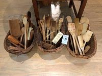 Three wicker baskets filled with an assortment of wooden kitchen utensils including spoons, forks, scissors, pasta strainer, whisk, and two reversible salad tongs.