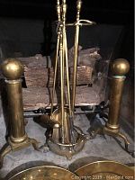 Photo shows the pair of brass fireplace andirons with ball and claw feet along with brass fireplace utensils arranged inside the hearth.