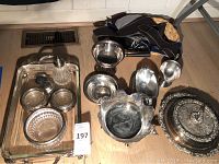 Overview of various silverplate and silver on bronze serving pieces on wooden floor including dishes, bowls, ashtrays, gravy boats, and a warming dish.