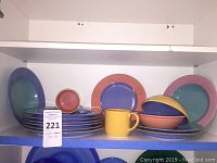 Photo of stacked plates, bowls, and mug showing variety of colors and sizes, with auction tag
