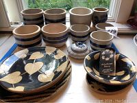 Multiple blue and cream striped clay containers and leaf patterned plates and bowls arranged on a table by a window.