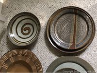 Top view of four ceramic plates and bowls with spiral, stripe, and banded earth-tone patterns on carpeted floor