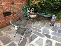 Full view of outdoor iron furniture set on stone patio next to brick wall, including chairs, tables, light, and garden hose.