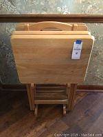 Front view of four wooden folding tray tables placed on a wooden stand.