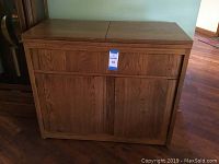 Front view of the wooden bar cabinet showing closed hinged lids on top, one drawer under the lids, and two doors below.