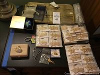 Top view of assorted jewelry, star pins in packaging, Estee Lauder box, rosary and cross, swan brooch, and Angel lapel pin